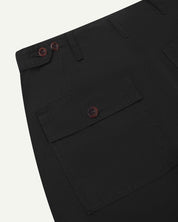 Close-up reverse view of Uskees black cotton work pants with focus on left rear pocket, belt loops, triple stitching and adjustable button waist.