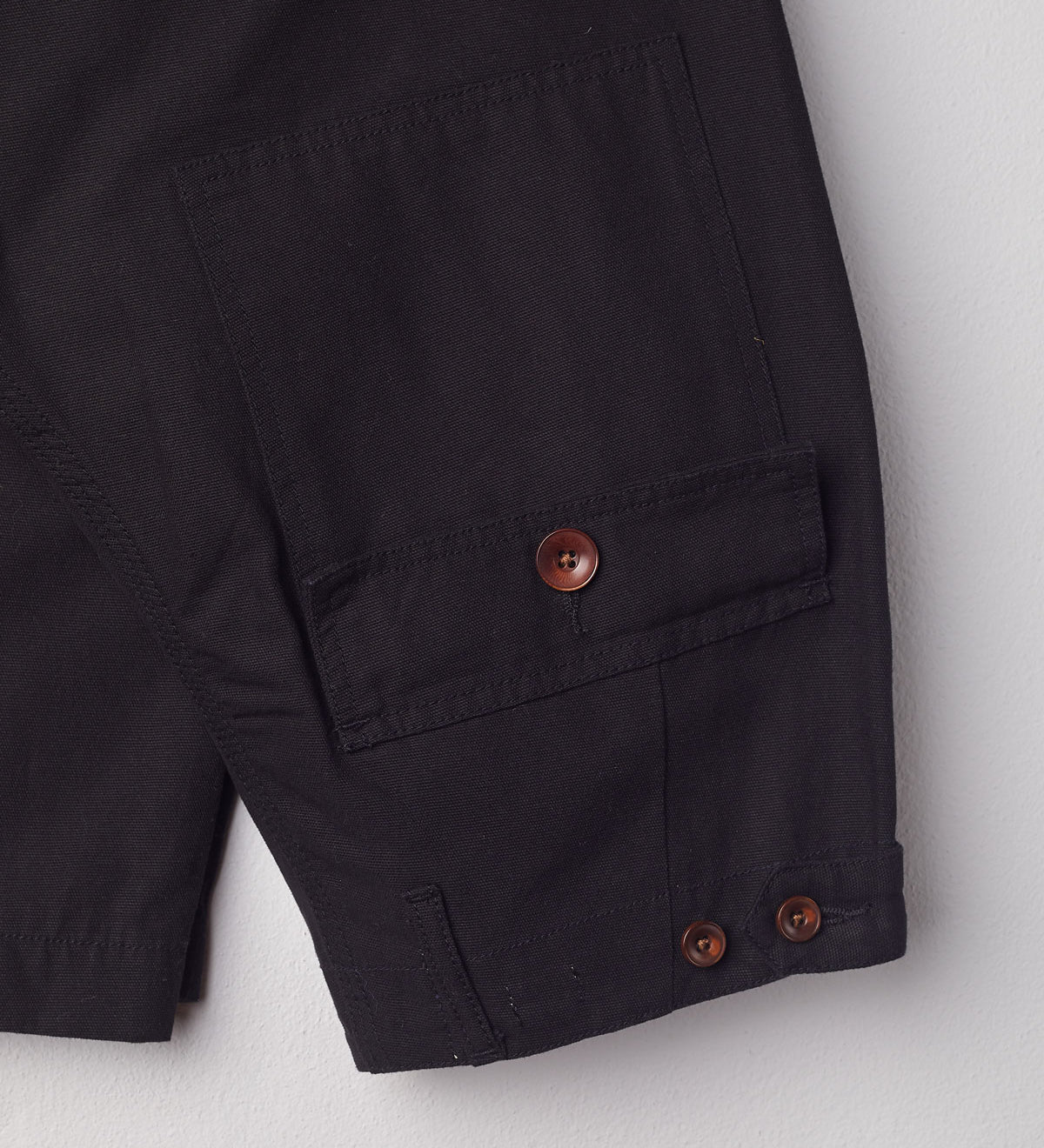 Close-up reverse view of Uskees discontinued black work pants with focus on natural corozo buttons, left rear pocket, belt loops, triple stitching and adjustable button waist.