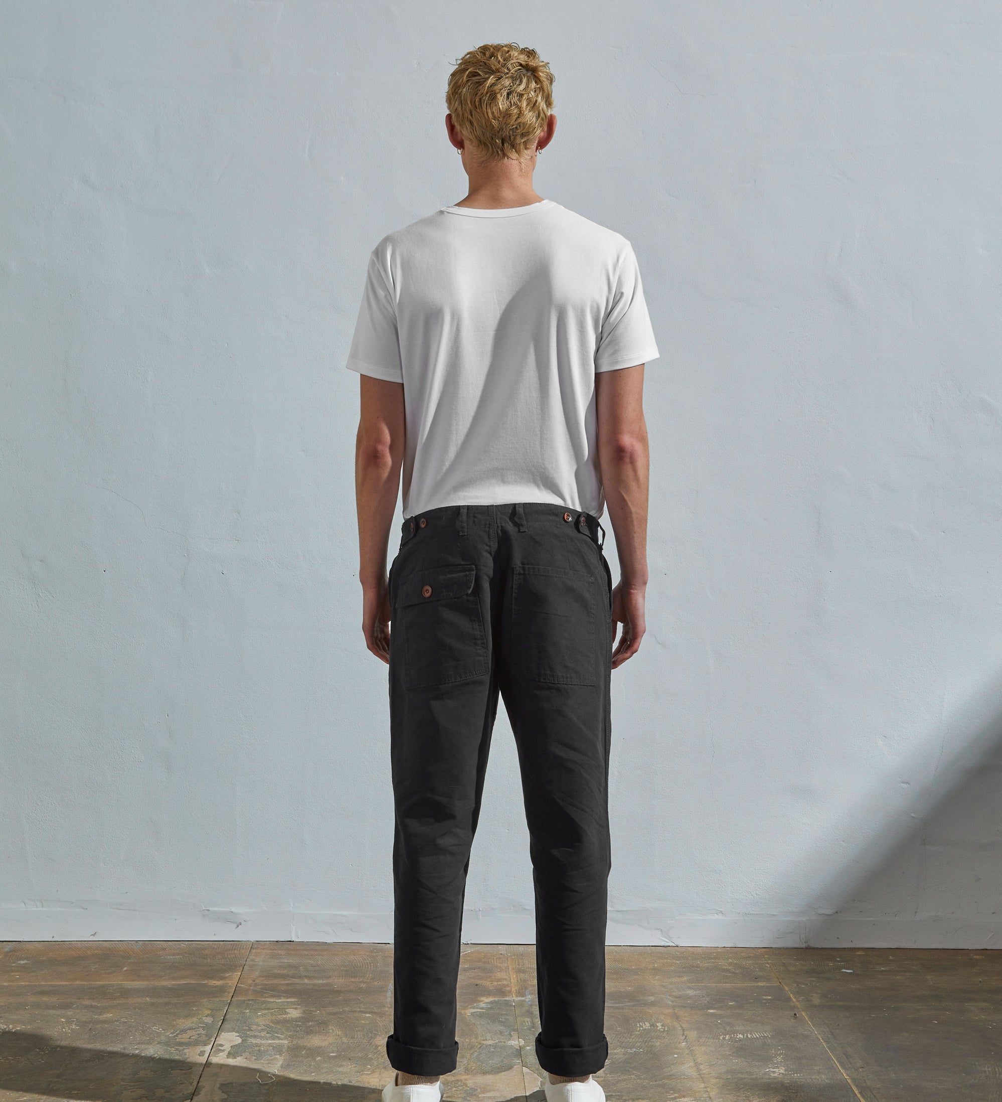 Full length back-view of model wearing discontinued black 5005 trousers with view of rear pockets and belt loops. Paired with plain white t-shirt.