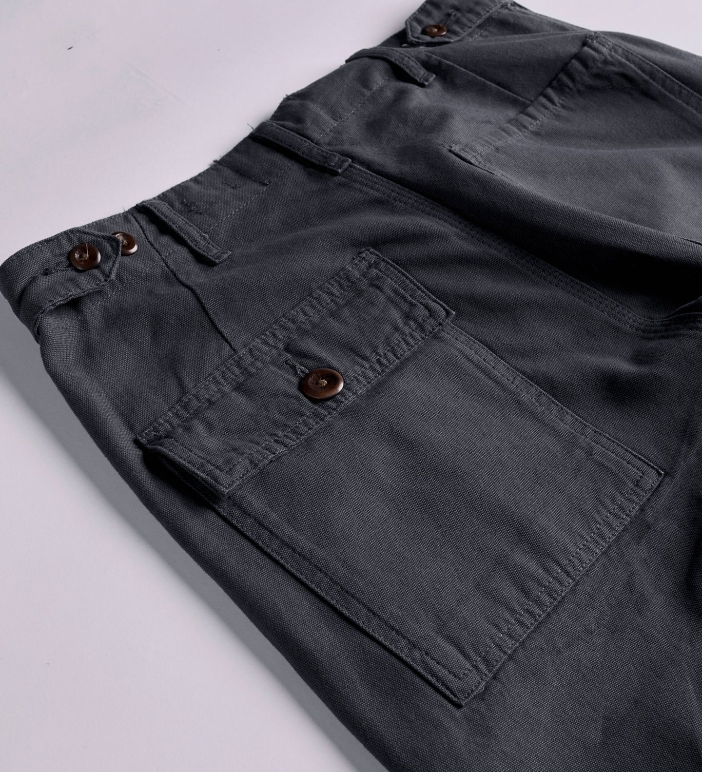 Close-up and angled reverse view of Uskees charcoal-grey cotton work pants with focus on left rear pocket, belt loops and triple stitching. Discontinued colour.