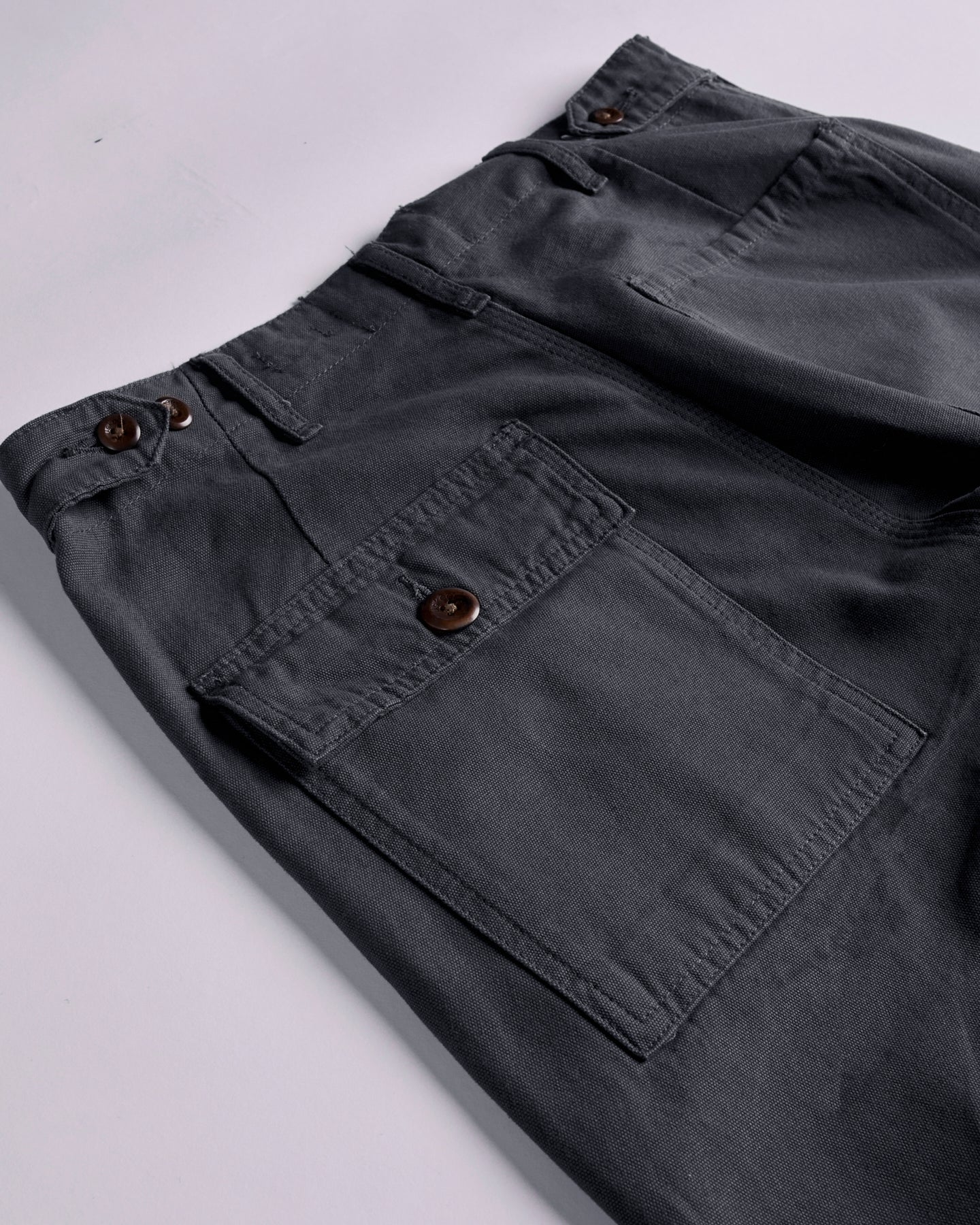 Close-up and angled reverse view of Uskees charcoal-grey cotton work pants with focus on left rear pocket, belt loops and triple stitching. Discontinued colour.