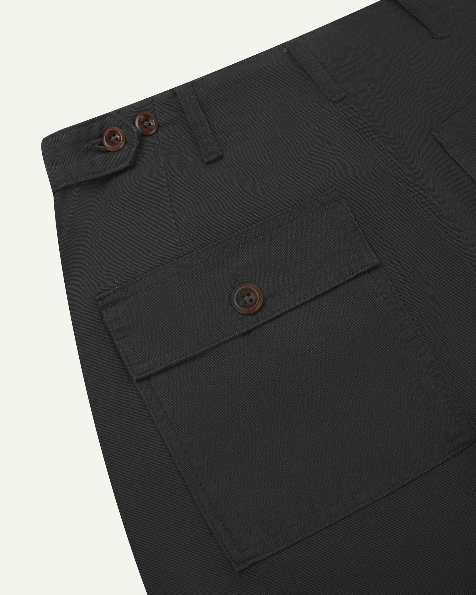 Close-up reverse view of Uskees charcoal-grey cotton work pants with focus on left rear pocket, belt loops, triple stitching and adjustable button waist.