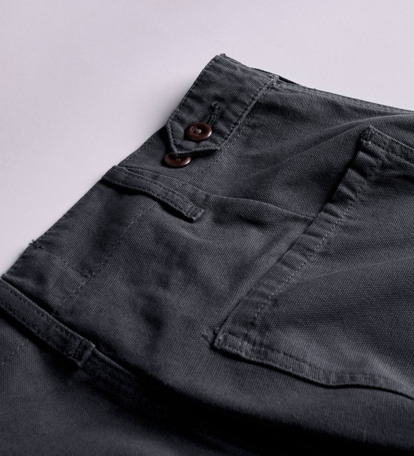 Close-up and angled reverse view of Uskees charcoal-grey cotton work pants with focus on right rear pocket and adjustable button waist. Discontinued colour.