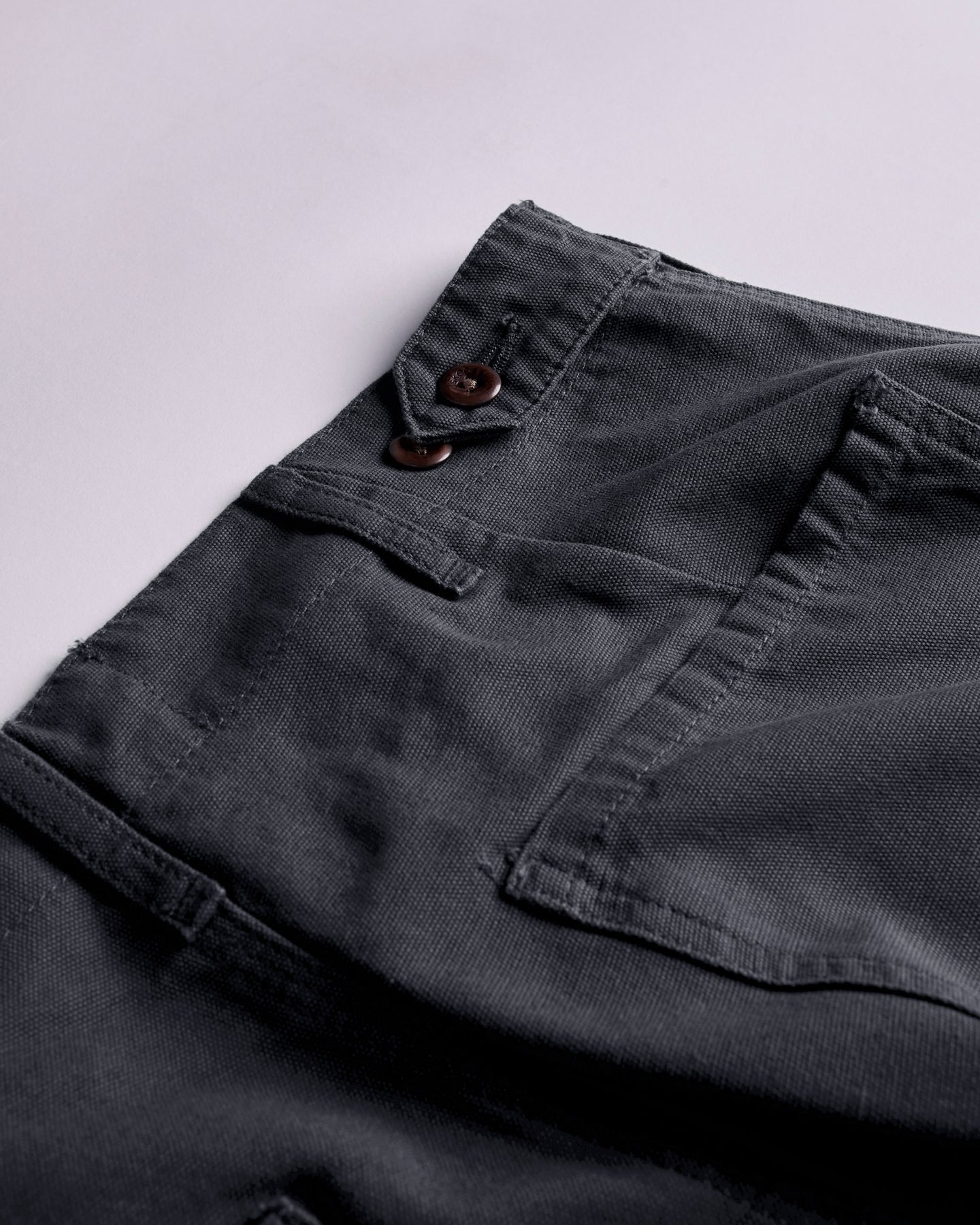 Close-up and angled reverse view of Uskees charcoal-grey cotton work pants with focus on right rear pocket and adjustable button waist. Discontinued colour.