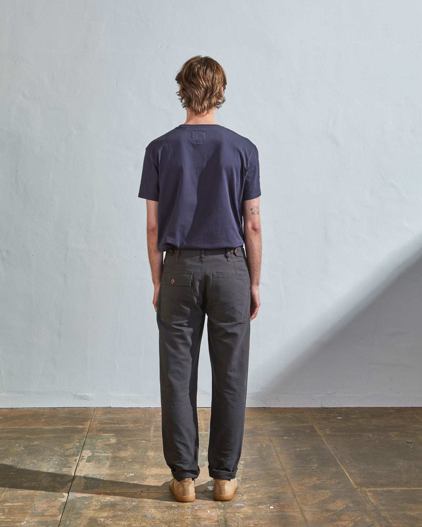Full length back-view of model wearing charcoal organic cotton #5005 trousers with view of rear and cargo pockets. Paired with midnight blue t-shirt.