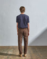 Full length back-view of model wearing chocolate organic cotton #5005 trousers with view of rear and cargo pockets. Paired with midnight blue t-shirt.