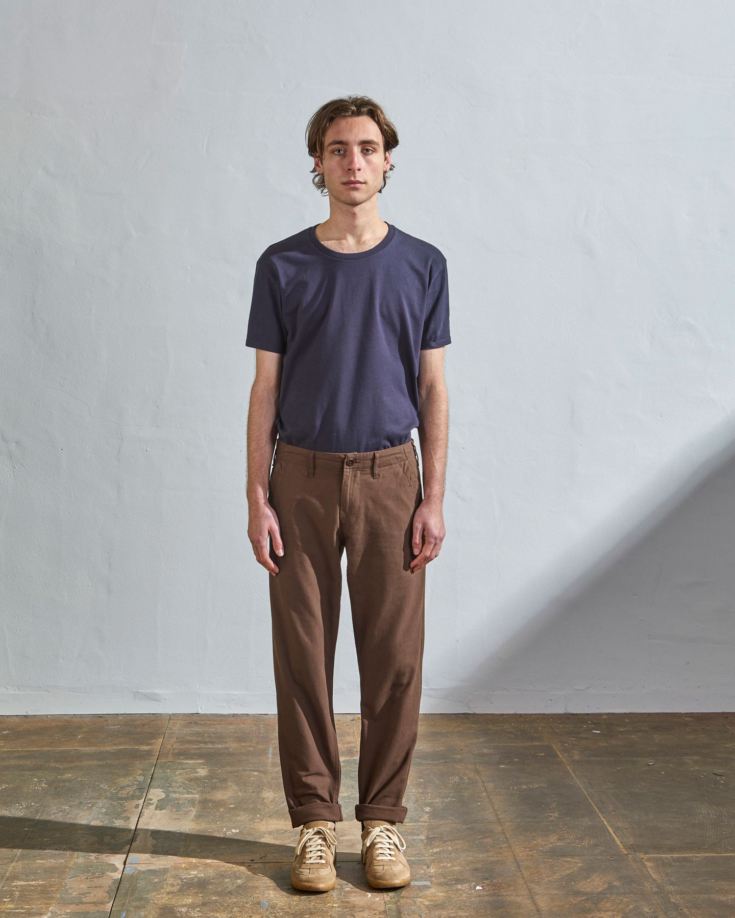 Full length front-view of model wearing chocolate cotton 5005 trousers with view of belt loops, cargo pockets and corozo buttons. Paired with midnight blue t-shirt.
