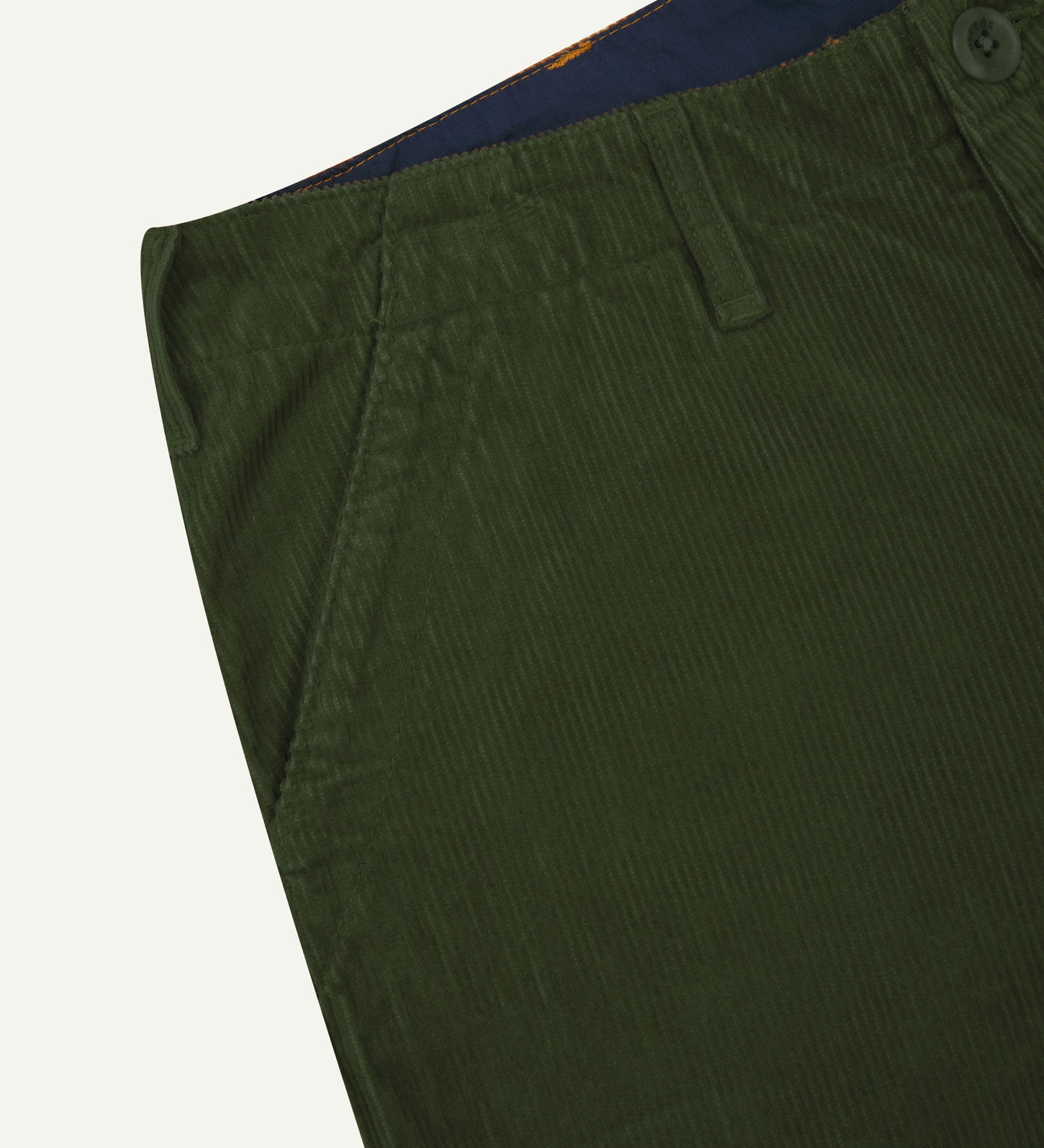 Close-up front view of left front pocket, belt loops, triple stitching, Corozo button and contrasting coloured lining material of coriander corduroy pants.