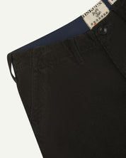 Close-up front view of left front pocket, belt loops, triple stitching, Corozo button and contrasting coloured lining material of faded black corduroy pants.