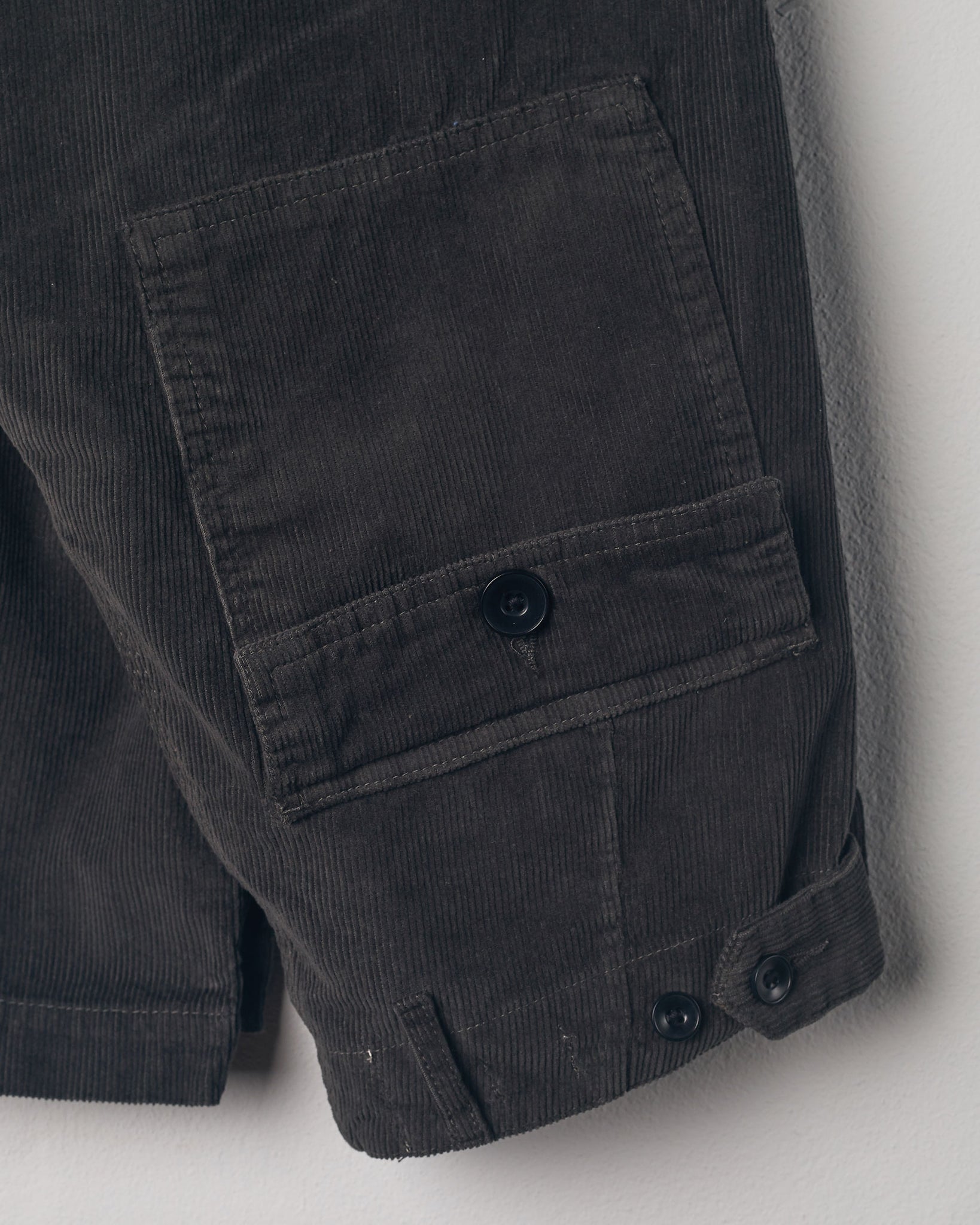 Close-up view of Uskees faded black corduroy work pants with focus on natural corozo buttons, left rear pocket, belt loops, triple stitching and adjustable button waist.