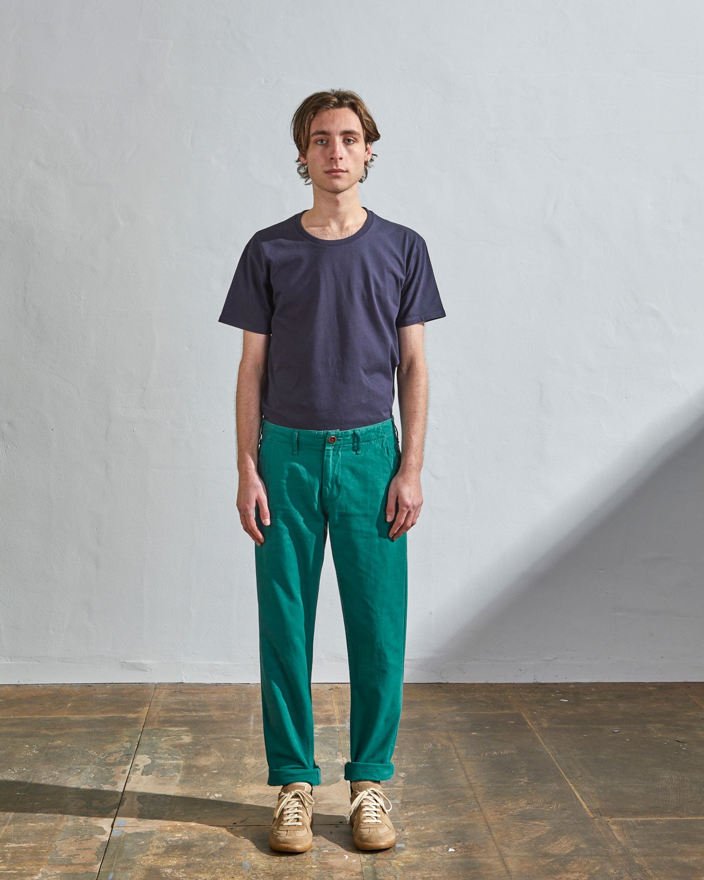 Full length front-view of model wearing foam green cotton 5005 trousers with view of belt loops, cargo pockets and Corozo buttons. Paired with midnight blue t-shirt.