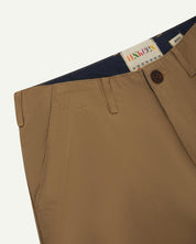 Close-up front view of left front pocket, belt loops, triple stitching, Corozo button and contrasting coloured lining material of khaki cotton pants.