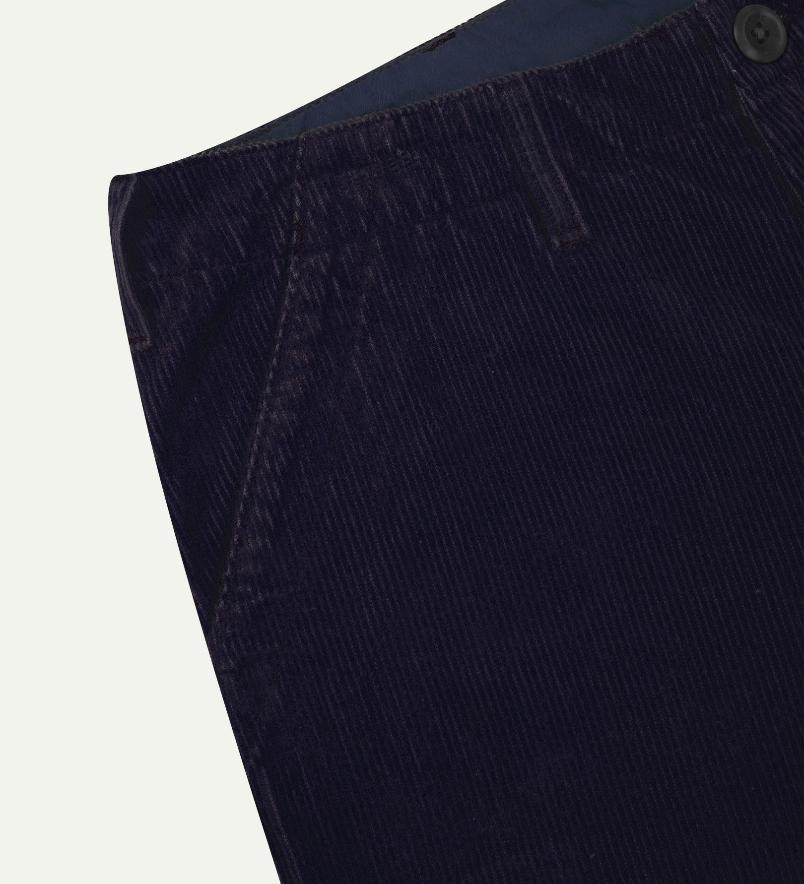 Close-up front view of left front pocket, belt loops, triple stitching, Corozo button and contrasting coloured lining material of midnight blue corduroy pants.