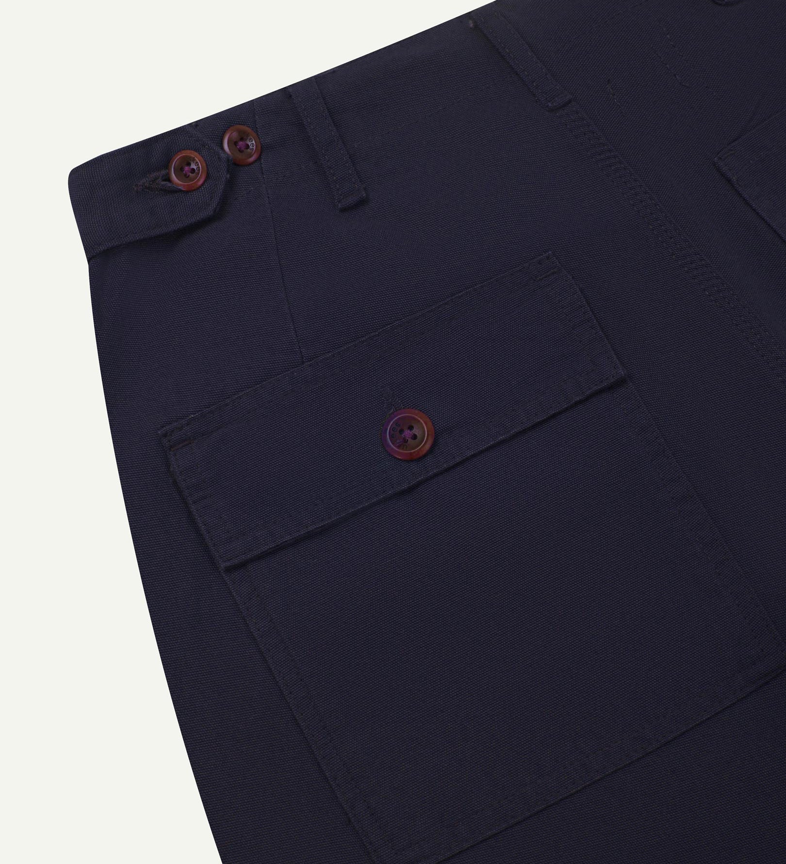 Close-up reverse view of Uskees midnight blue cotton work pants with focus on left rear pocket, belt loops, triple stitching and adjustable button waist.