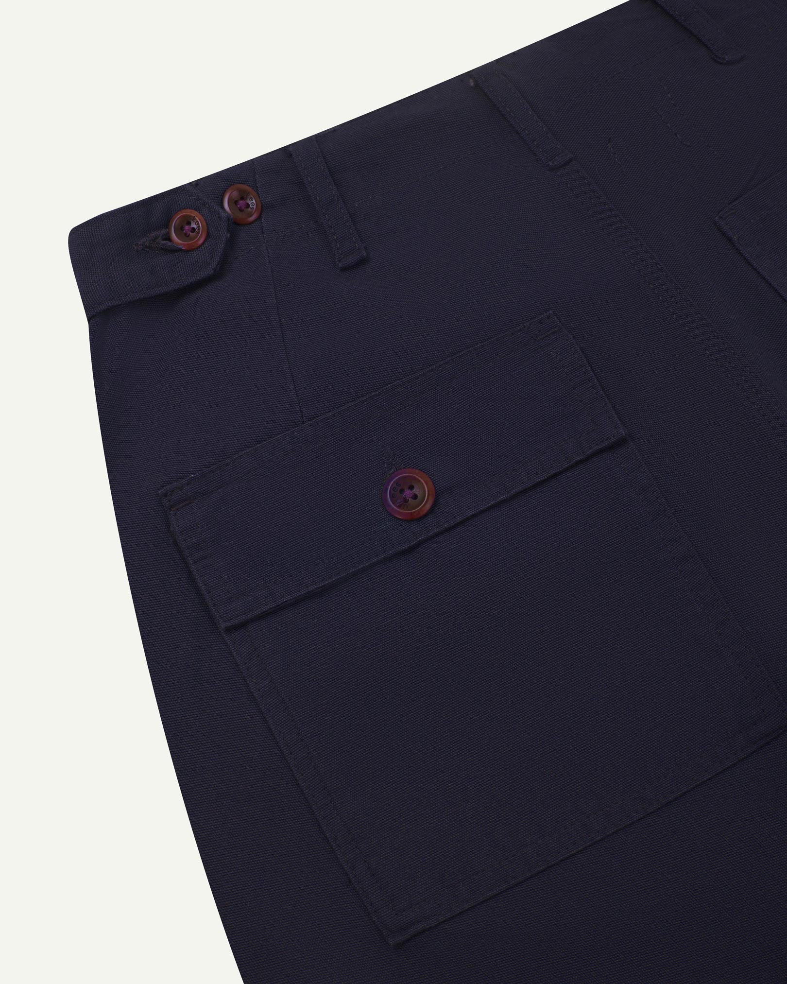 Close-up reverse view of Uskees midnight blue cotton work pants with focus on left rear pocket, belt loops, triple stitching and adjustable button waist.