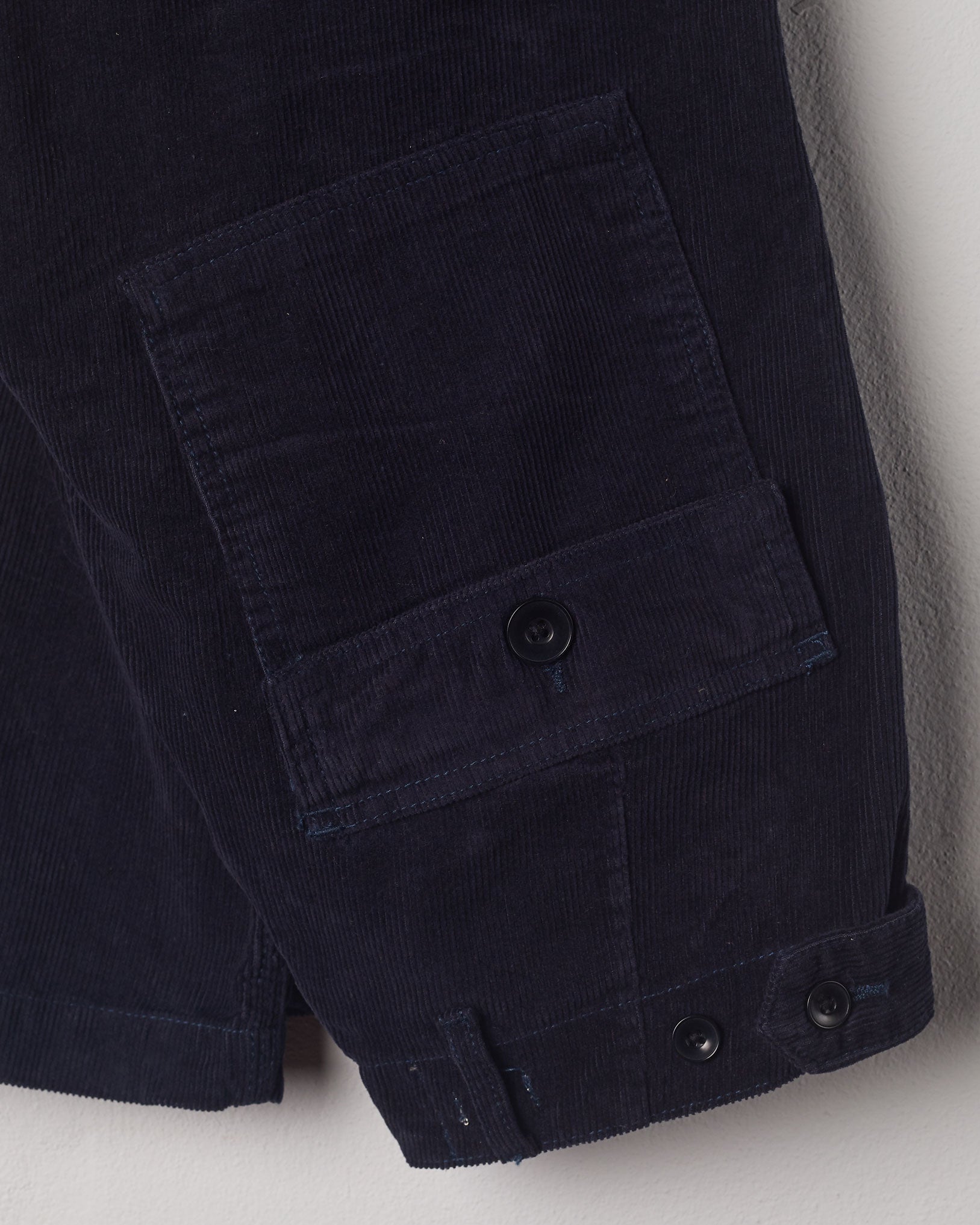Close-up view of Uskees midnight blue corduroy work pants with focus on natural corozo buttons, left rear pocket, belt loops, triple stitching and adjustable button waist.