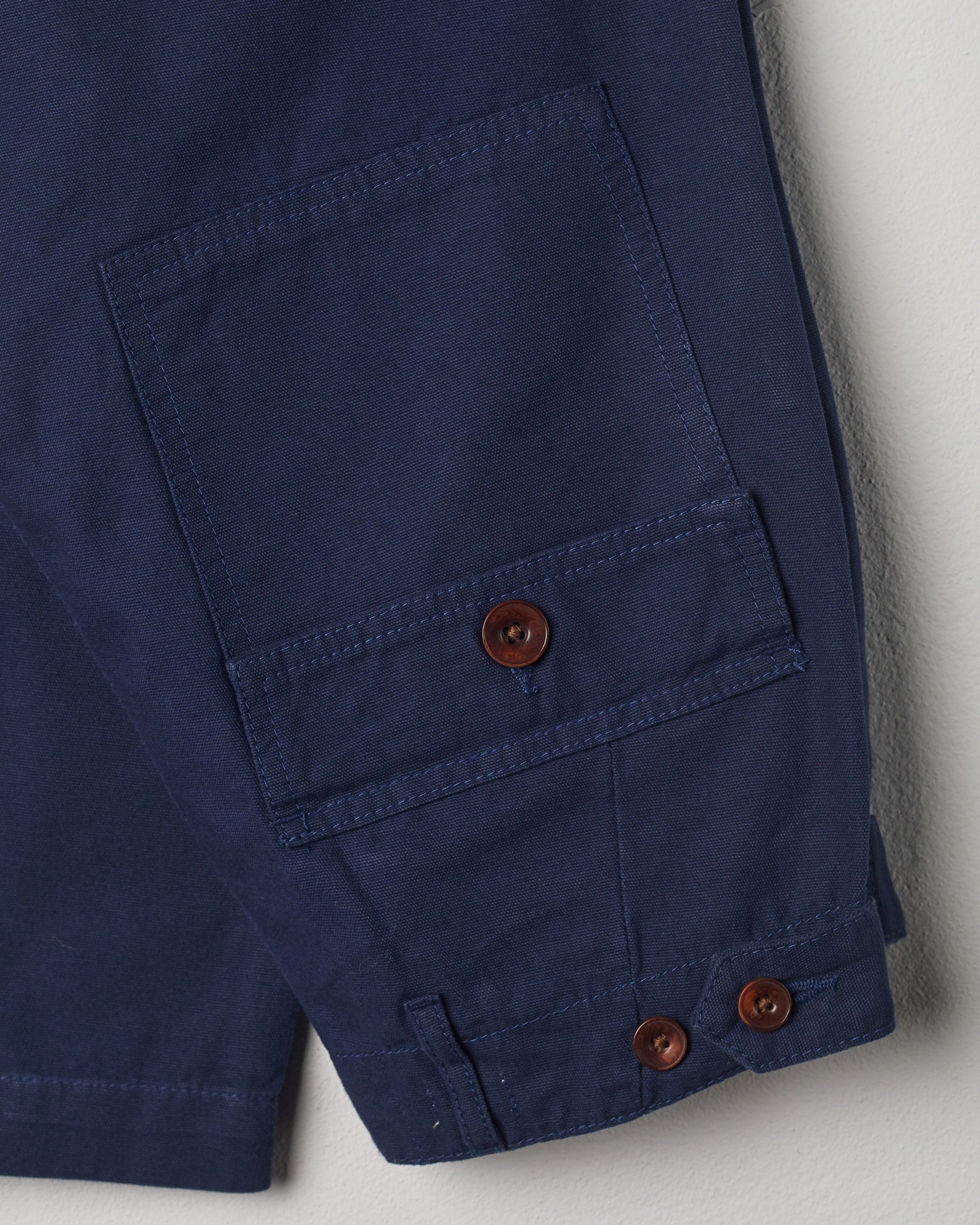 Close-up view of Uskees navy work pants with focus on natural corozo buttons, left rear pocket, belt loops, triple stitching and adjustable button waist.