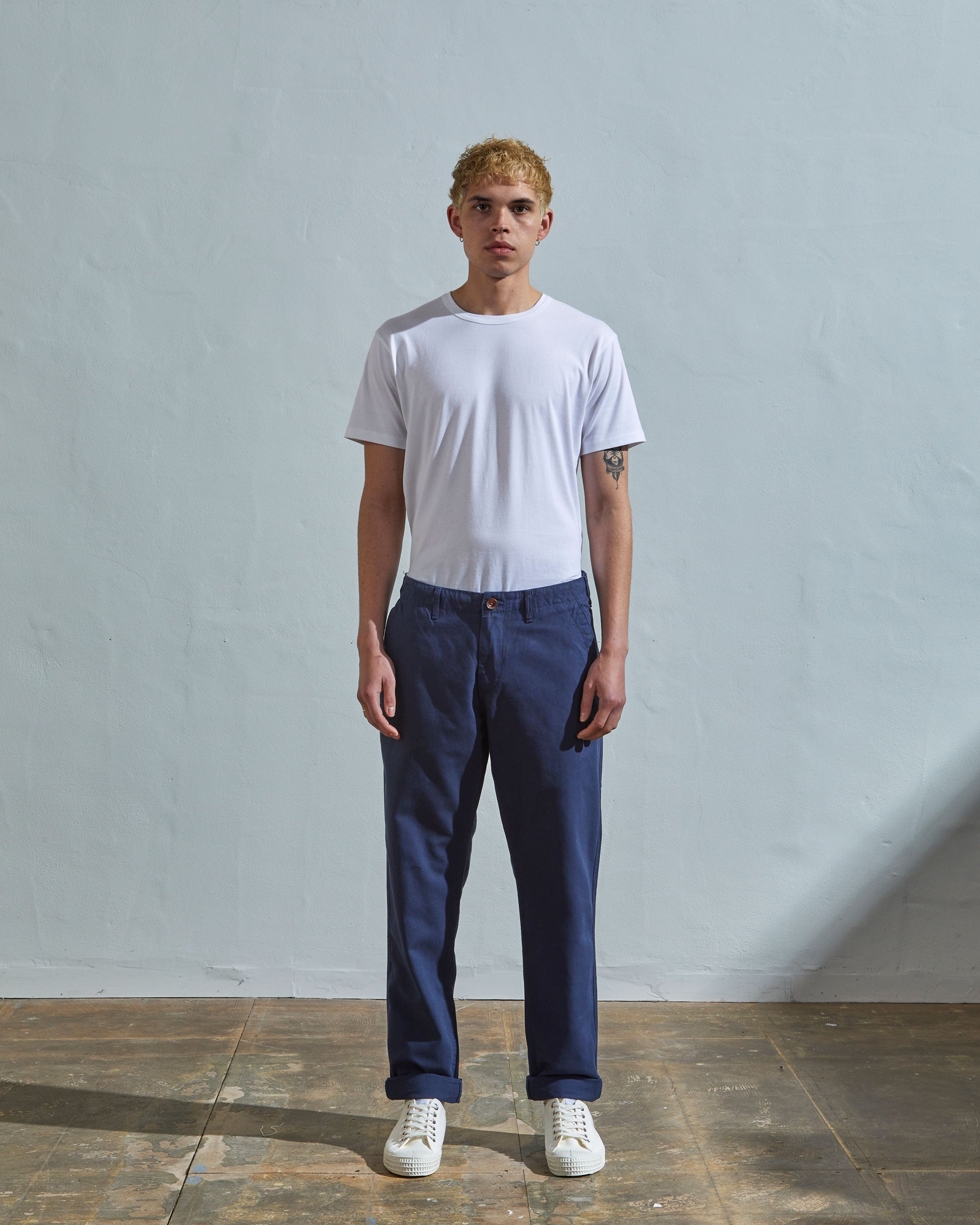 Full length front-view of model wearing navy blue 5005 trousers with view of YKK zip fly and Corozo buttons. Paired with plain white t-shirt.