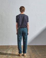 Full length back-view of model wearing peacock green-blue organic cotton #5005 trousers with view of rear and cargo pockets. Paired with midnight blue t-shirt.