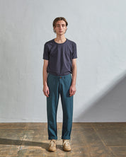 Full length front-view of model wearing peacock cotton 5005 trousers with view of belt loops, cargo pockets and Corozo buttons. Paired with midnight blue t-shirt.
