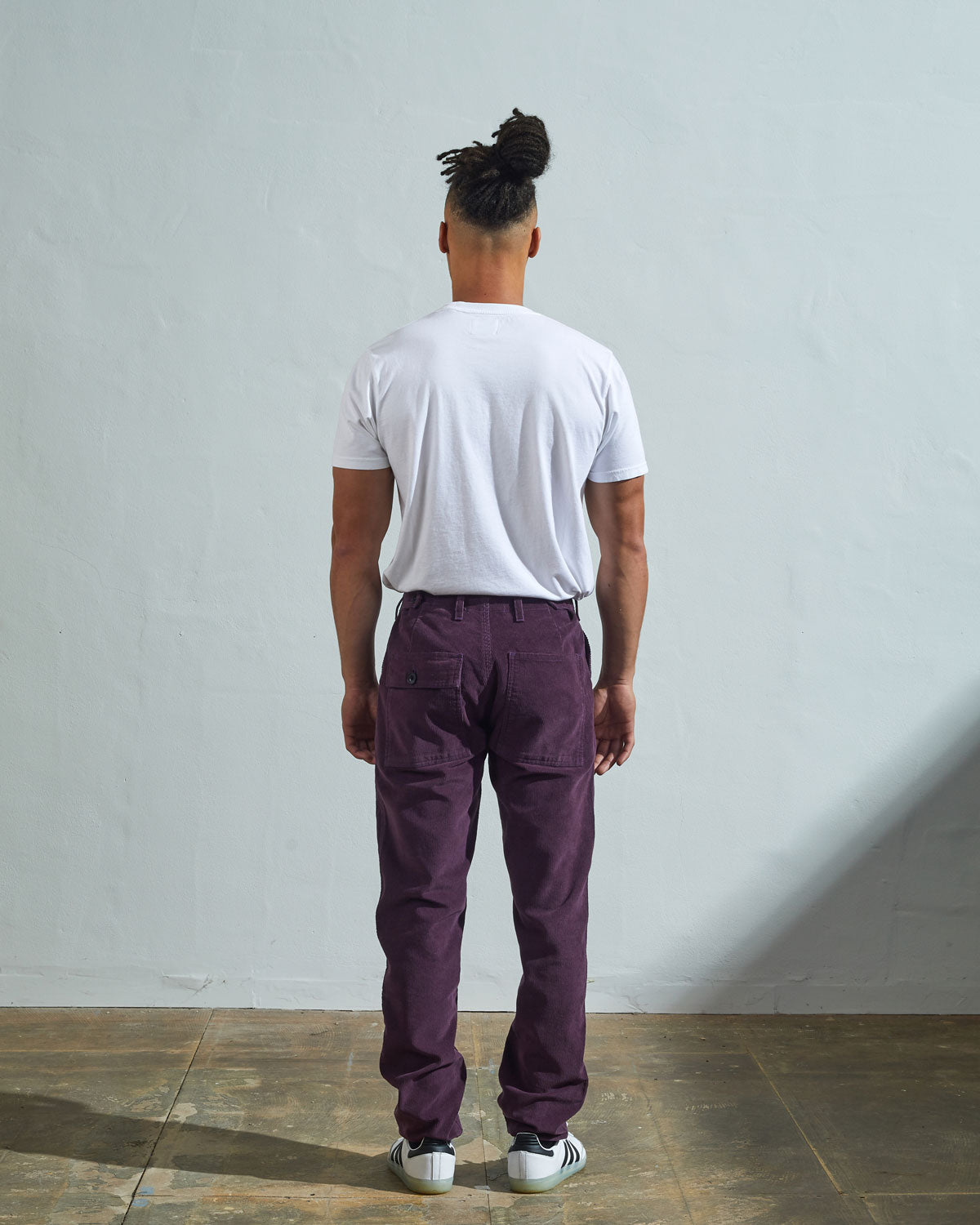 Full length back-view of model wearing purple-plum corduroy 5005 trousers with view of rear pockets and belt loops. Paired with plain white t-shirt.