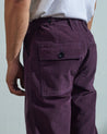 Close-up view of Uskees purple-plum corduroy work pants with focus on natural corozo buttons, left rear pocket, belt loops, triple stitching and adjustable button waist.