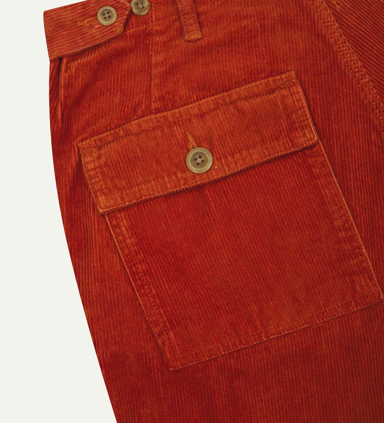 Close-up reverse view of Uskees rust-red corduroy work pants with focus on left rear flap pocket, belt loops and adjustable button waist.