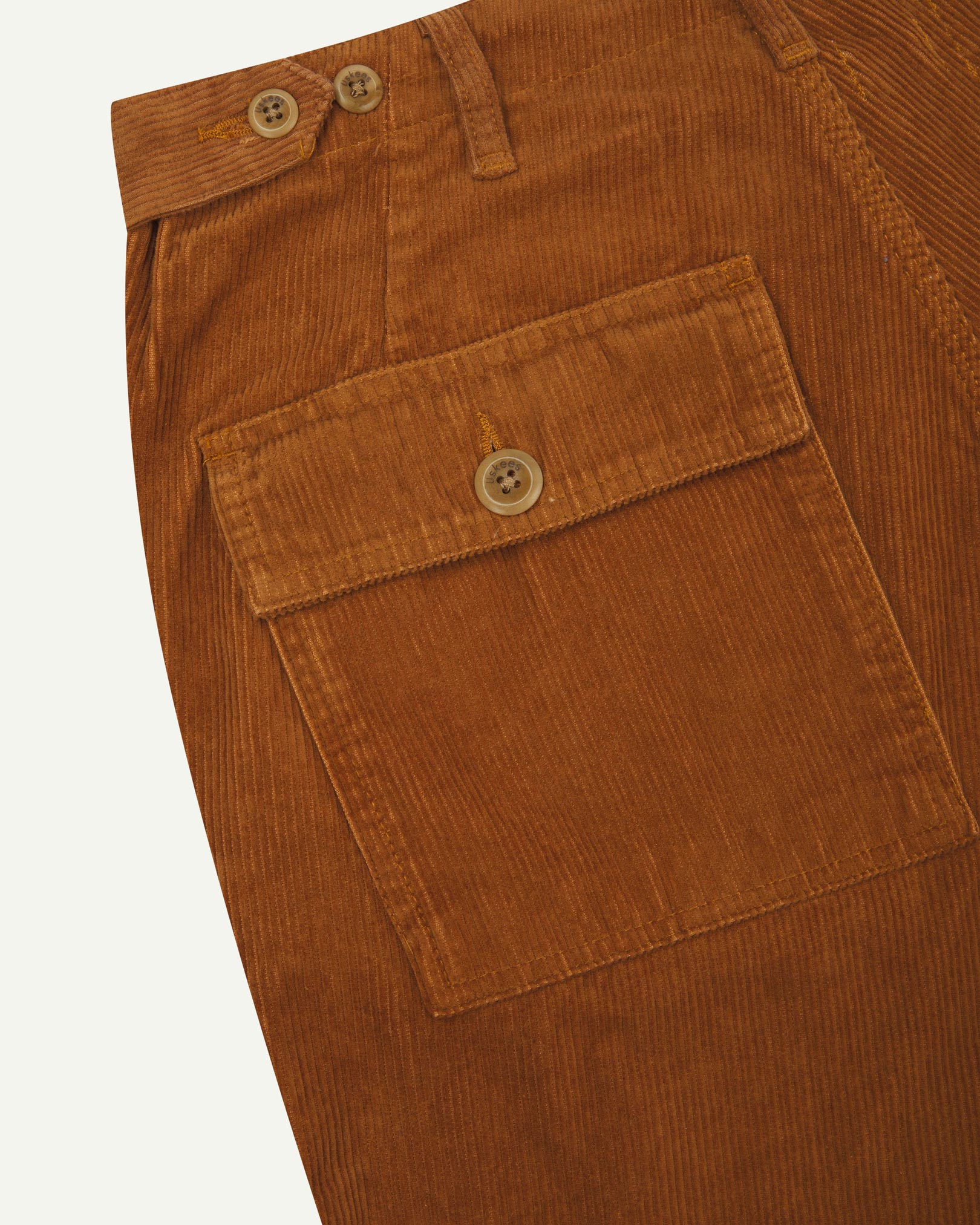 Close-up reverse view of Uskees tan corduroy work pants with focus on left rear pocket, belt loops, triple stitching and adjustable button waist.