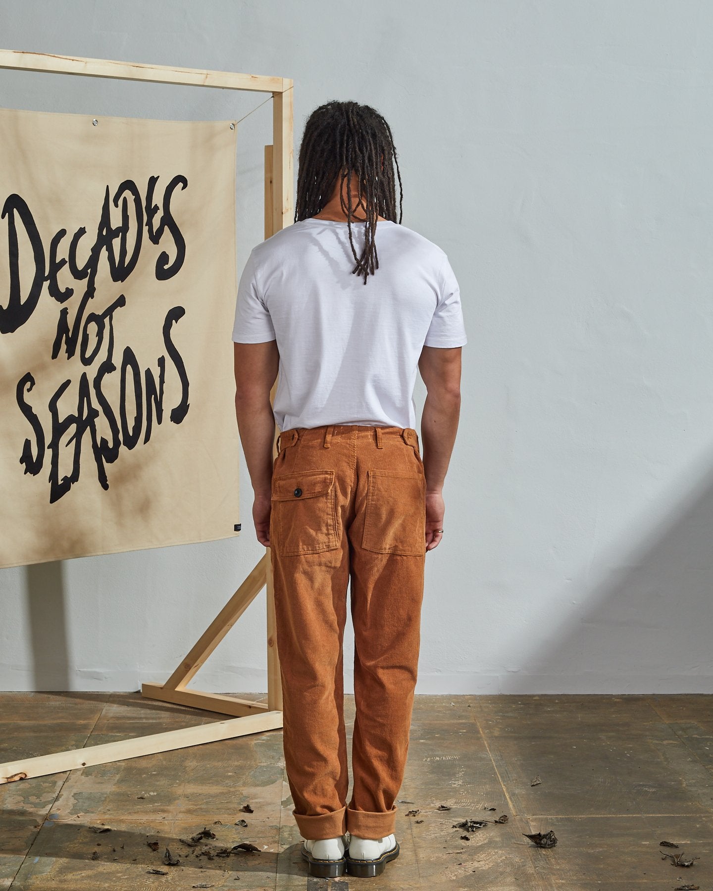 Full length front-view of model wearing tan corduroy 5005 trousers with view of YKK zip fly and Corozo buttons. Paired with plain white t-shirt.