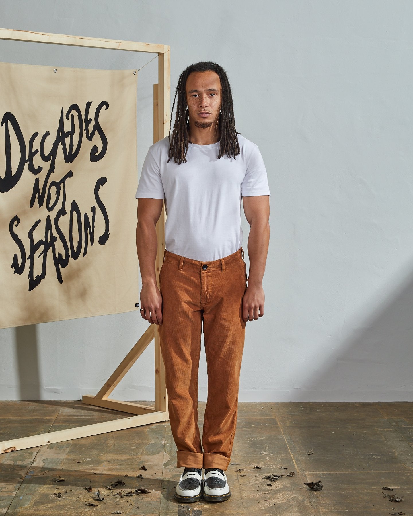 Full length back-view of model wearing tan corduroy 5005 trousers with view of rear pockets and belt loops. Paired with plain white t-shirt.