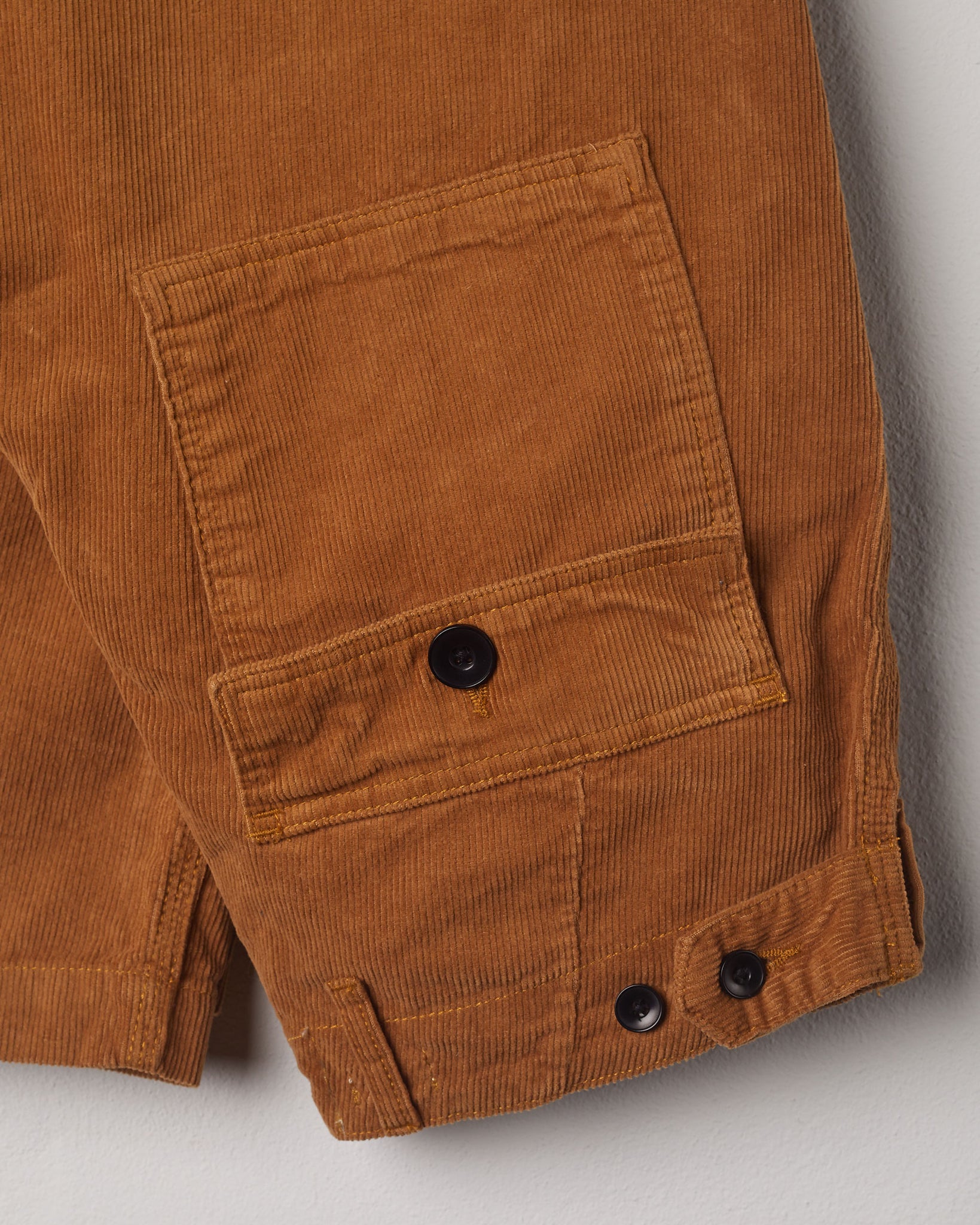 Close-up view of Uskees tan corduroy work pants with focus on natural corozo buttons, left rear pocket, belt loops, triple stitching and adjustable button waist.