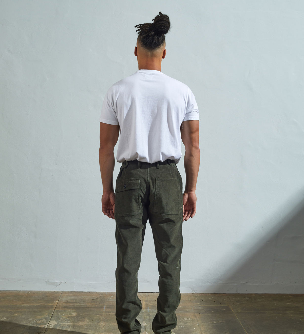 Full length back-view of model wearing vine green corduroy 5005 trousers with view of rear pockets and belt loops. Paired with plain white t-shirt.