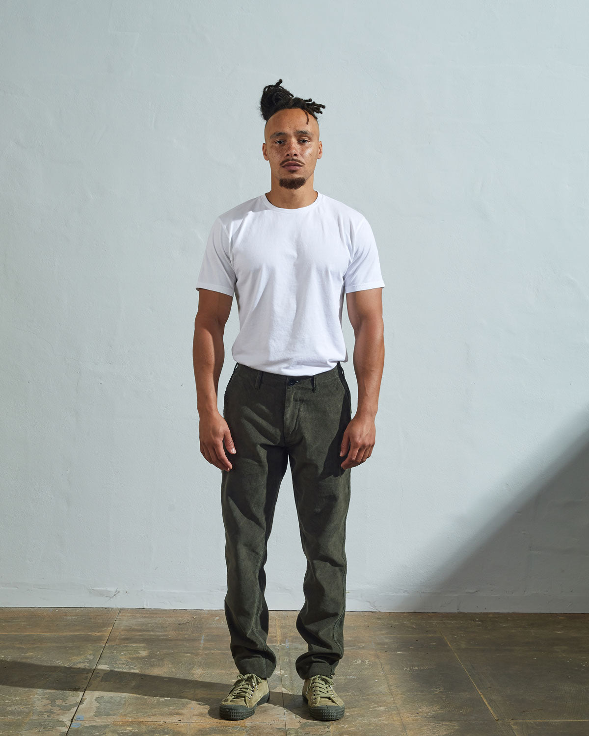 Full length front-view of model wearing vine green corduroy 5005 trousers with view of YKK zip fly and Corozo buttons. Paired with plain white t-shirt.