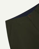 Close-up front view of left front pocket, belt loops, triple stitching, Corozo button and contrasting coloured lining material of vine green cotton pants.