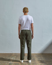 Full length back-view of model wearing vine green 5005 trousers with view of rear pockets and belt loops. Paired with plain white t-shirt.