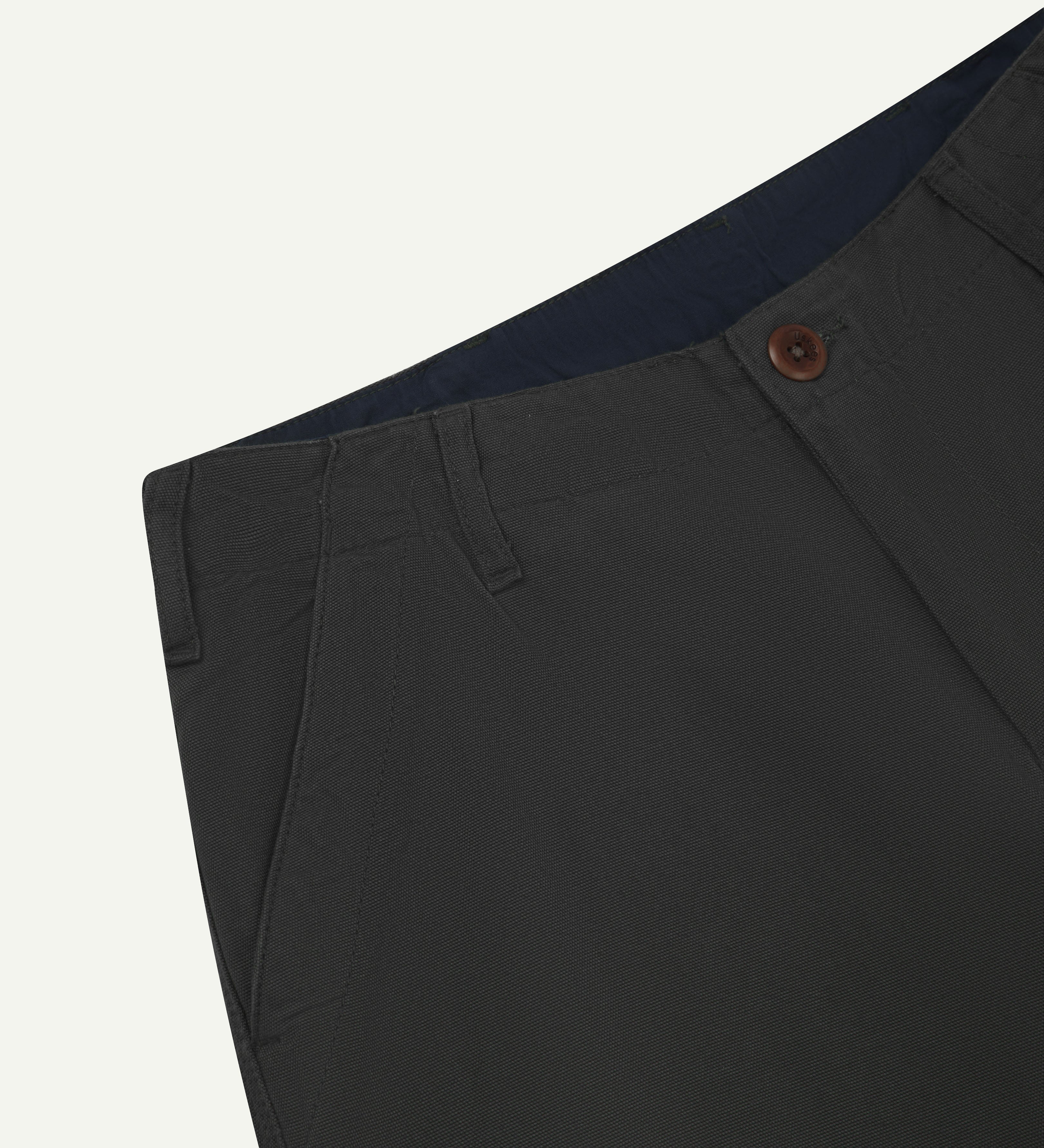 Close up view of uskees #5005 men's trousers in dark grey showing lined waist, front pocket, button fastening and belt loops