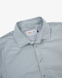 Close-up front view of pale blue-grey Technique trekking shirt for men showing the collar area with front ticket pocket, branding label and hanging loop.
