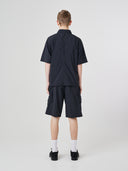 Full-length back view of a male model wearing an Uskees black short-sleeve button front trek shirt paired with matching Uskees technical shorts.