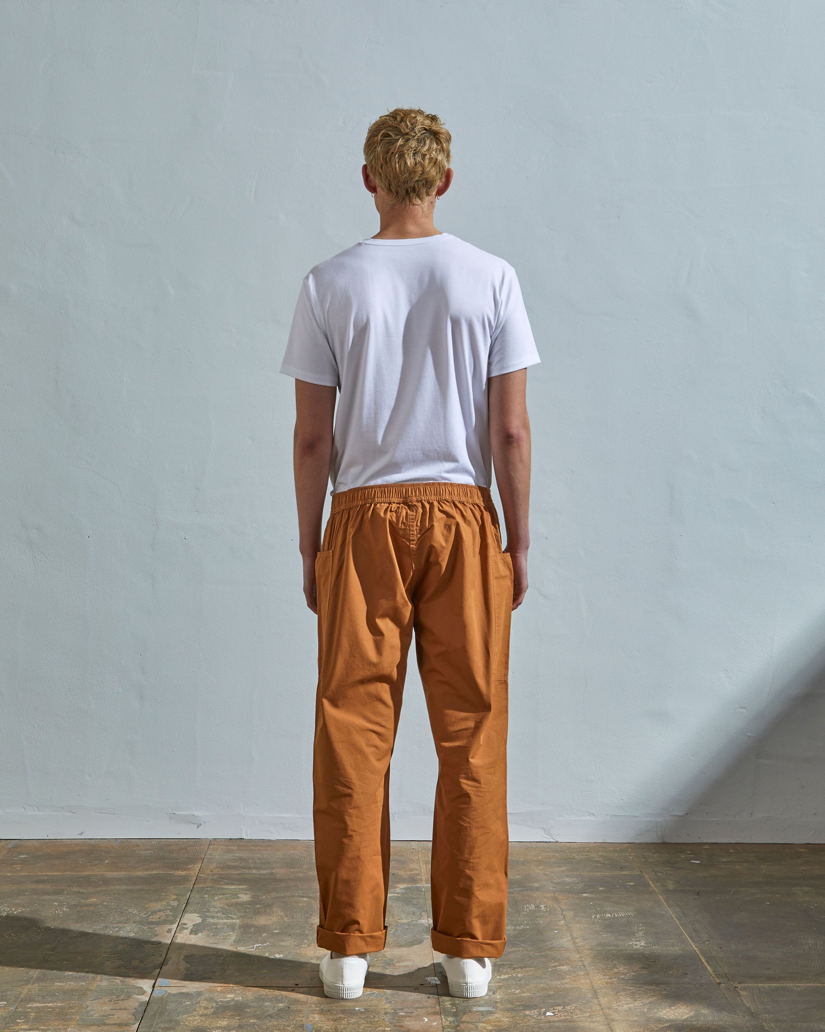 Full length back-view of model wearing pale brown lightweight cotton 5011 trousers showing the relaxed, tapered fit on the leg and turn-ups.