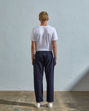 Full length back-view of model wearing midnight blue lightweight cotton 5011 trousers showing the relaxed, tapered fit on the leg and turn-ups.