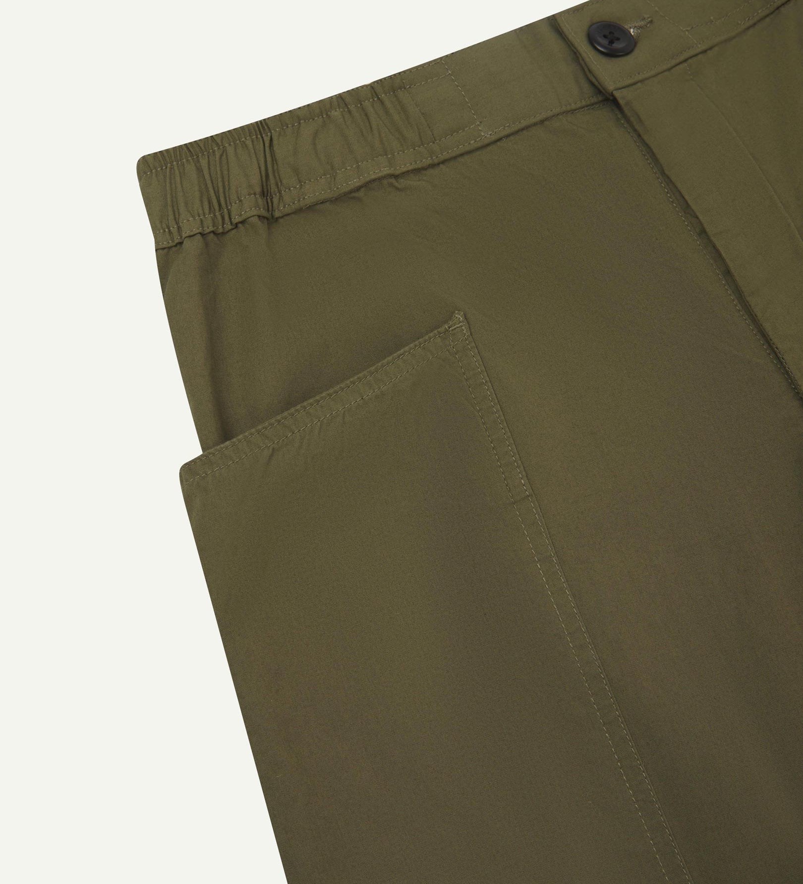Close angled view of the elasticated waist and corozo button fastening and pockets of the olive green 5011 Uskees pants.