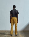 Full length reverse view of model wearing citronella-yellow corduroy 5012 trousers with view of straight leg fit, rear pockets and belt loops.