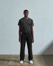 Full length front-view of model wearing faded black corduroy 5012 trousers with view of straight leg silhouette and Corozo buttons. Paired with matching t-shirt.