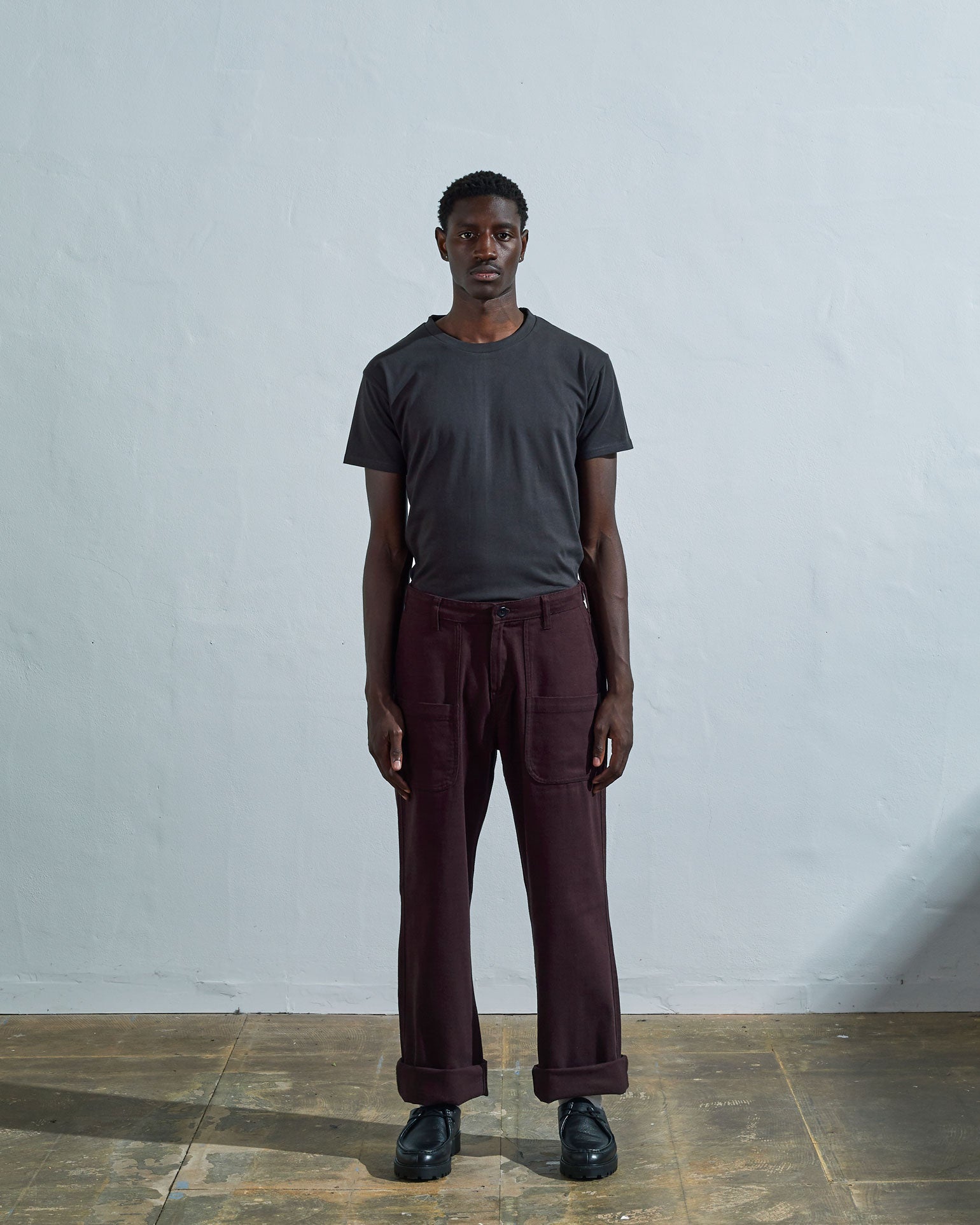 Full-length front view of model wearing #5013 drill commuter pants in dark plum with turn-ups, paired with Uskees faded black tee.