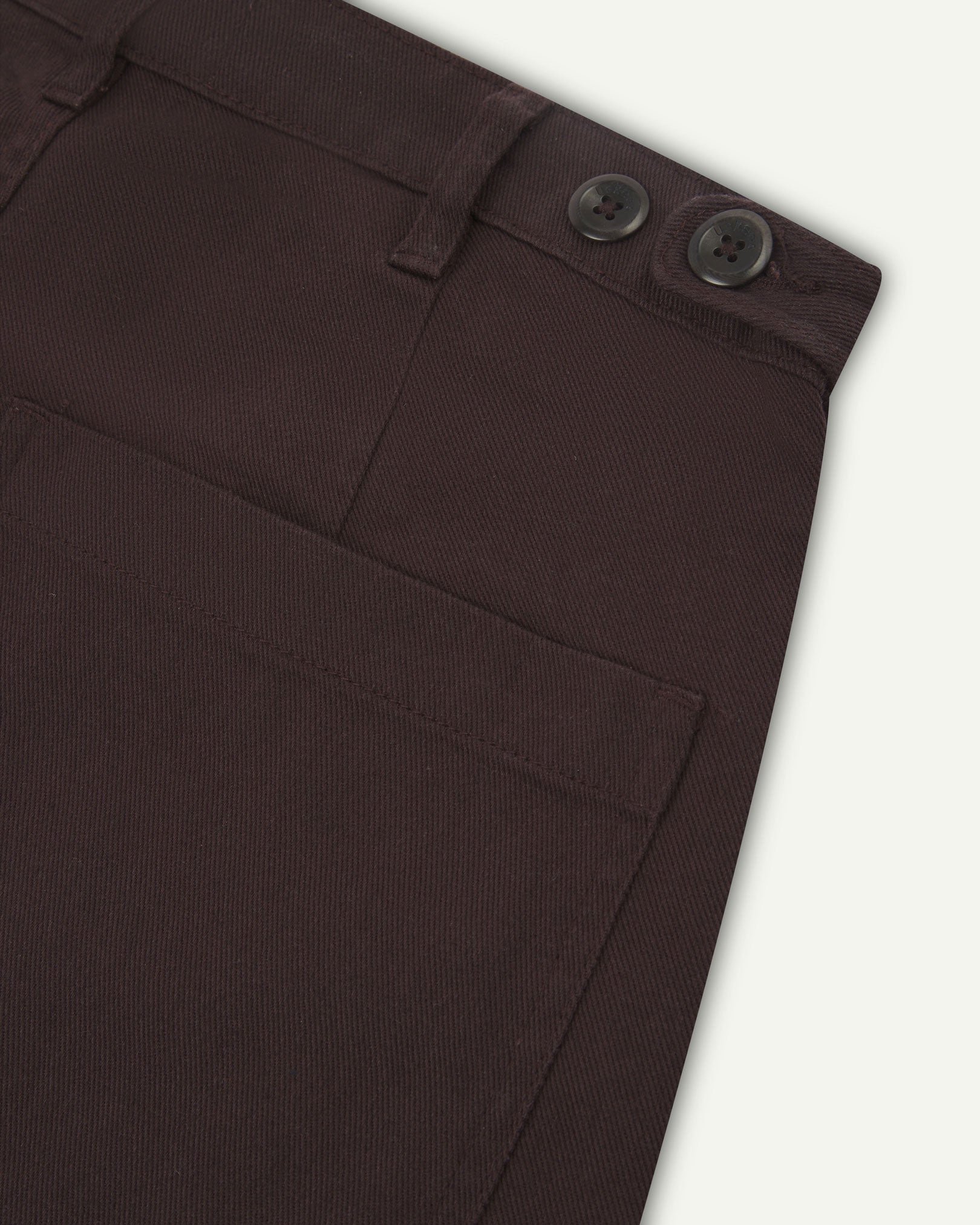 Reverse close-up of 5013 Uskees drill straight leg pants in brown-maroon, with focus on left rear pocket, belt loops and adjustable waistband with corozo buttons.