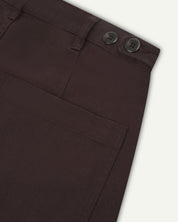 Reverse close-up of 5013 Uskees drill straight leg pants in brown-maroon, with focus on left rear pocket, belt loops and adjustable waistband with corozo buttons.