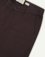 Front close-up of 5013 Uskees drill straight leg pants in brown-maroon, with focus on front pockets, layered pockets, belt loops waistband and Uskees branding label.