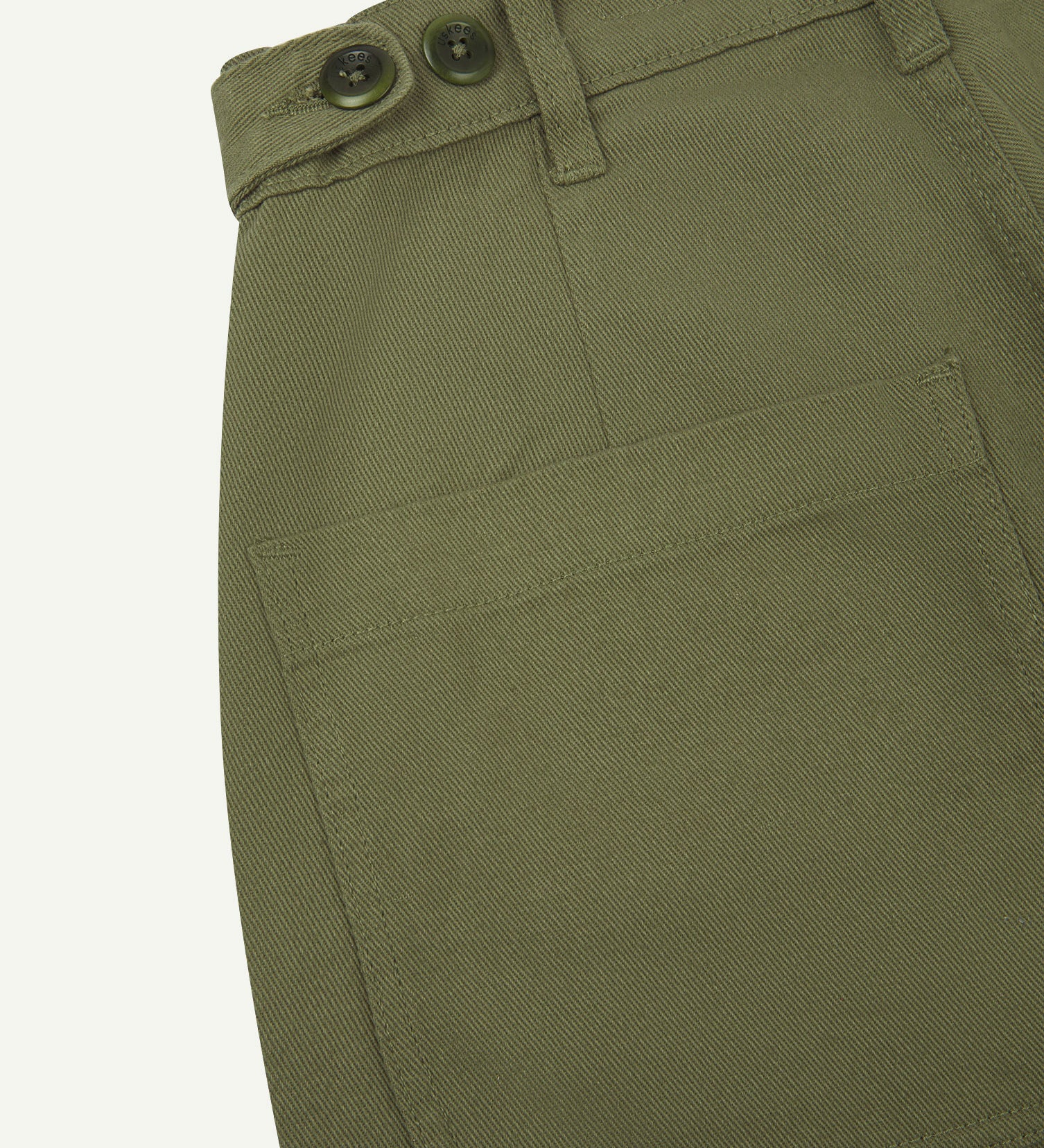 Reverse close-up of 5013 Uskees drill straight leg pants in moss green, with focus on left rear pocket, belt loops and adjustable waistband with corozo buttons.