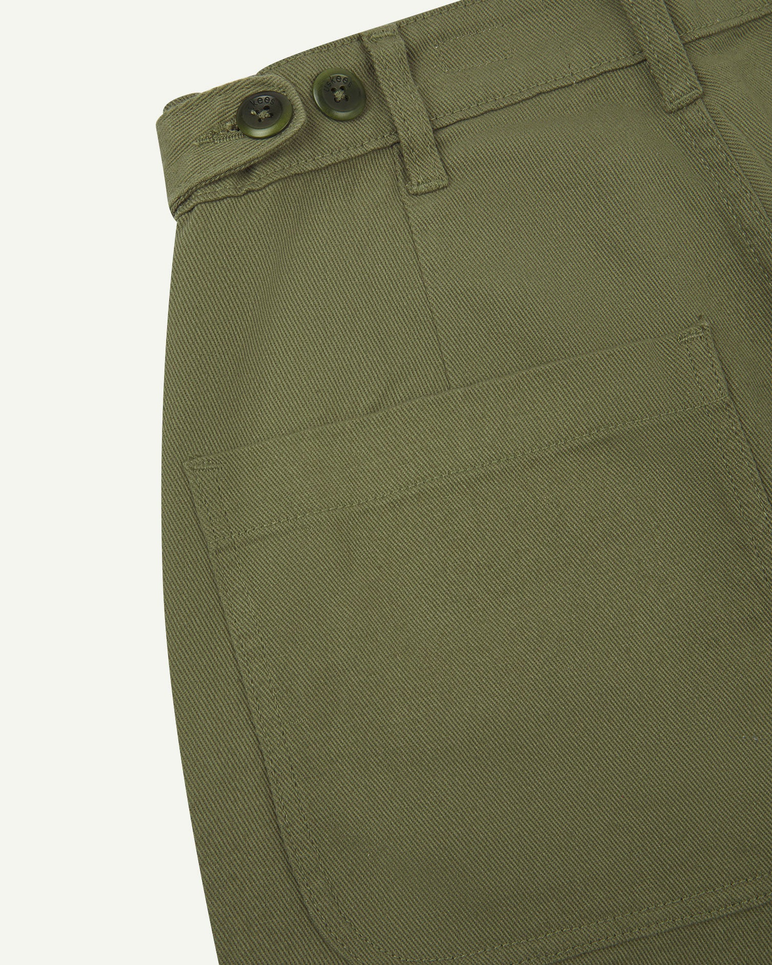 Reverse close-up of 5013 Uskees drill straight leg pants in moss green, with focus on left rear pocket, belt loops and adjustable waistband with corozo buttons.