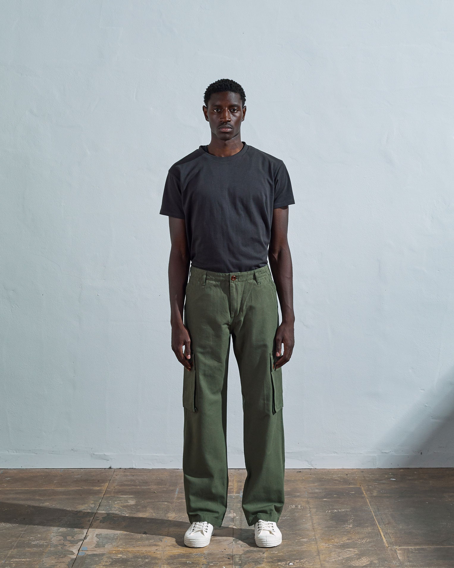 Full length front-view of model wearing coriander-green cotton 5014 trousers with view of belt loops, cargo pockets and Corozo buttons.